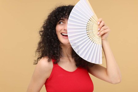 Foto de Mujer feliz sosteniendo ventilador de mano sobre fondo beige - Imagen libre de derechos