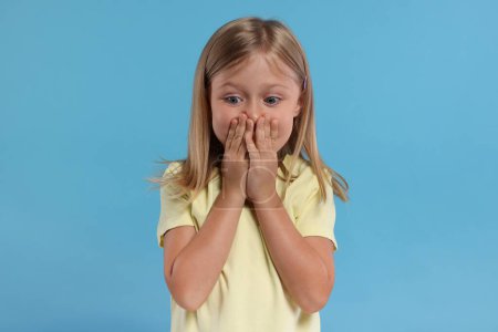 Photo for Embarrassed little girl covering mouth with hands on light blue background - Royalty Free Image
