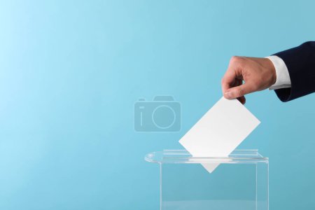 Photo for Man putting his vote into ballot box on light blue background, closeup. Space for text - Royalty Free Image