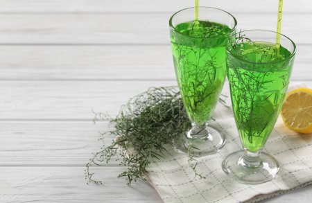 Photo for Glasses of homemade refreshing tarragon drink, sprigs and lemon on white wooden table, space for text - Royalty Free Image