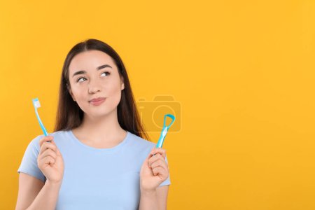 Beautiful woman with tongue cleaner and plastic toothbrush on yellow background, space for text