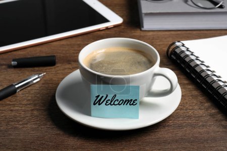 Téléchargez les photos : Note collante avec mot Bienvenue attaché à une tasse de café sur un bureau en bois - en image libre de droit