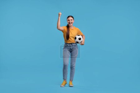 Photo for Happy soccer fan with ball celebrating on light blue background - Royalty Free Image