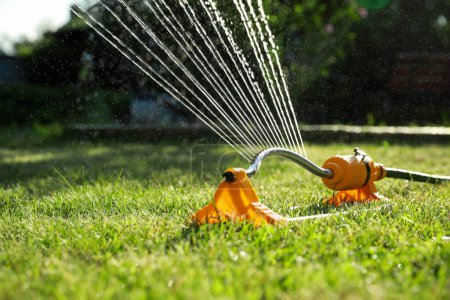 Foto de Aspersor automático que riega la hierba verde en el césped en el jardín. Sistema de riego - Imagen libre de derechos