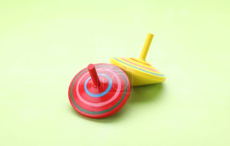 Photo for Two bright spinning tops on light green background, closeup. Toy whirligig - Royalty Free Image