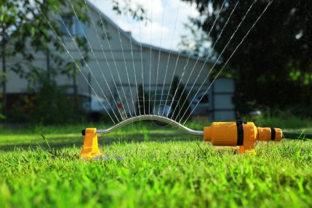 Foto de Aspersor automático que riega la hierba verde en el césped en el jardín. Sistema de riego - Imagen libre de derechos
