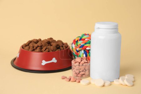 Téléchargez les photos : Vitamines, jouets et aliments secs pour animaux dans un bol sur fond beige - en image libre de droit