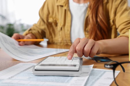 Woman calculating taxes at wooden table in room, closeup