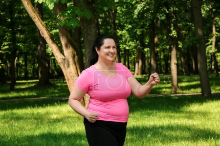 Téléchargez les photos : Heureuse femme en surpoids faisant de l'exercice dans le parc - en image libre de droit