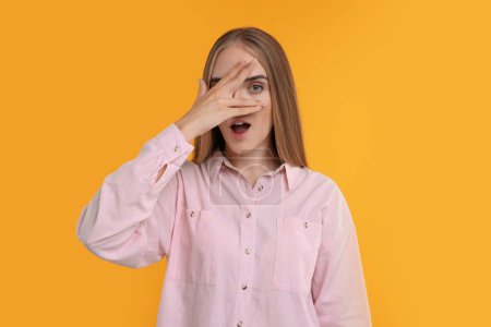 Photo for Embarrassed woman covering face with hand on orange background - Royalty Free Image