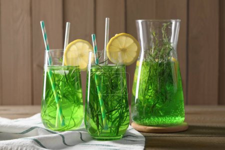 Photo for Jug and glasses of refreshing tarragon drink with lemon slices on wooden table - Royalty Free Image