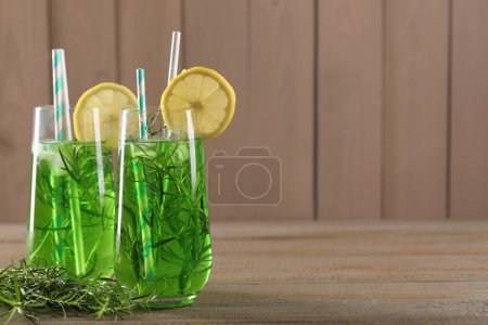Photo for Glasses of refreshing tarragon drink with lemon slices on wooden table, space for text - Royalty Free Image