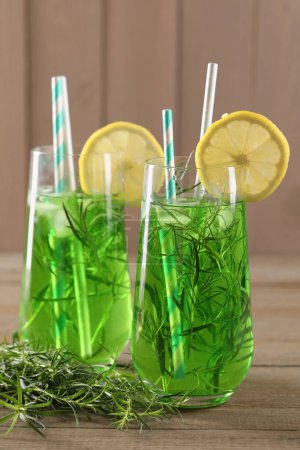 Photo for Glasses of refreshing tarragon drink with lemon slices on wooden table - Royalty Free Image
