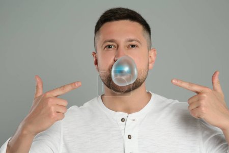 Photo for Handsome man blowing bubble gum on light grey background - Royalty Free Image