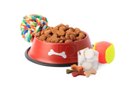 Téléchargez les photos : Aliments secs pour animaux dans un bol, vitamines et jouets isolés sur blanc - en image libre de droit