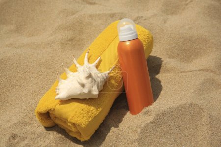 Photo for Sunscreen, seashell and rolled towel on sandy beach. Sun protection - Royalty Free Image