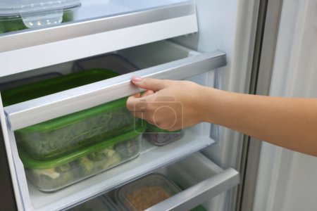 Photo for Woman pulling out fridge drawer with different fresh products, closeup. Food storage - Royalty Free Image