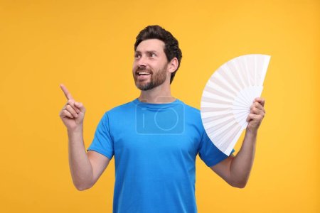 Foto de Hombre feliz sosteniendo ventilador de mano sobre fondo naranja - Imagen libre de derechos