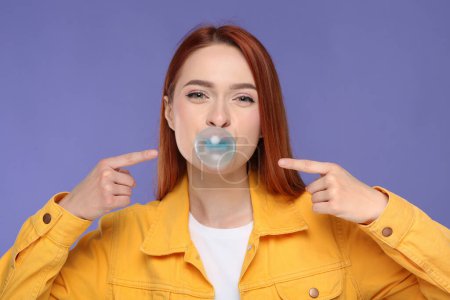 Téléchargez les photos : Belle femme soufflant gomme à bulles sur fond violet - en image libre de droit