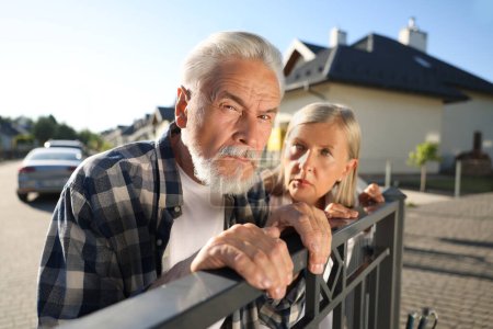 Téléchargez les photos : Concept de vie privée. Curieux couple de personnes âgées espionnant les voisins au-dessus de la clôture à l'extérieur - en image libre de droit
