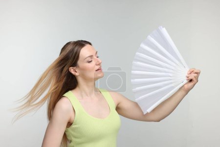 Foto de Hermosa mujer agitando ventilador de mano blanco para refrescarse sobre fondo gris claro - Imagen libre de derechos