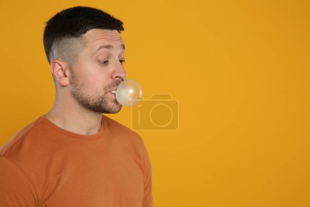 Téléchargez les photos : Homme surpris soufflant de la gomme à bulles sur fond orange, espace pour le texte - en image libre de droit