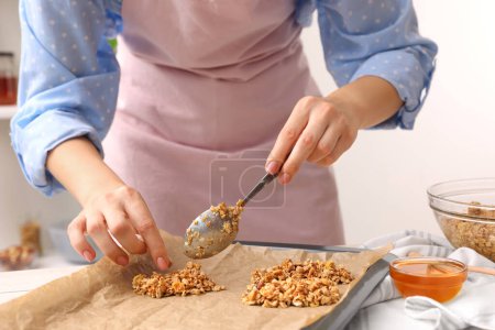 Faire des barres de granola. Femme mettant un mélange de flocons d'avoine, de fruits secs et d'autres ingrédients sur une plaque de cuisson à table dans la cuisine, gros plan