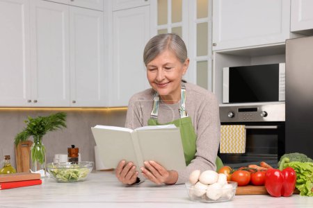 Foto de Mujer feliz con libro de recetas en la mesa en la cocina - Imagen libre de derechos