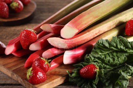 Téléchargez les photos : Couper les tiges fraîches de rhubarbe et les fraises sur une table en bois, gros plan - en image libre de droit