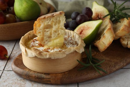 Leckerer gebackener Brie-Käse, Brot und andere Produkte auf hellem Kacheltisch