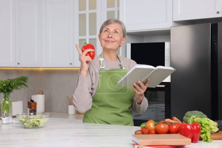 Foto de Mujer feliz con libro de recetas y pimiento en la cocina - Imagen libre de derechos