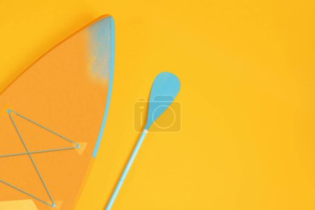 Photo for Board and paddle on orange background, flat lay with space for text. Standup paddleboarding (SUP) - Royalty Free Image