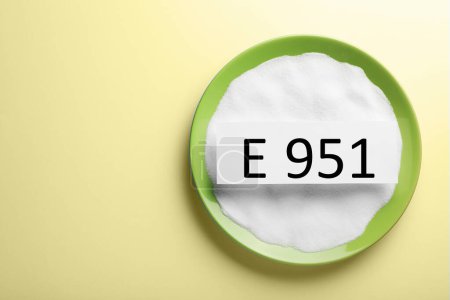 Foto de Tarjeta con código de aspartamo (E951) y edulcorante artificial en bol sobre fondo amarillo, vista superior. Espacio para texto - Imagen libre de derechos