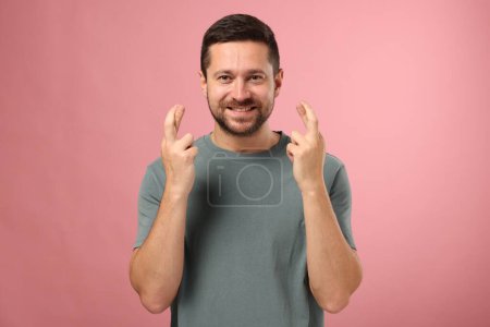 Foto de Hombre feliz cruzando sus dedos sobre fondo rosa - Imagen libre de derechos