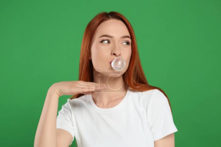 Photo for Beautiful woman blowing bubble gum on green background - Royalty Free Image