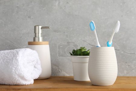 Téléchargez les photos : Brosses à dents en plastique dans le support, serviette, plante en pot et produit cosmétique sur table en bois - en image libre de droit