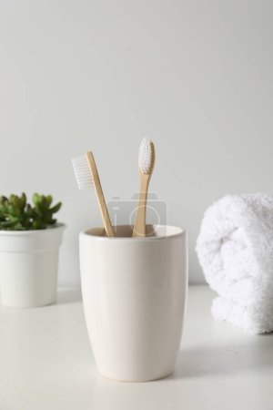 Téléchargez les photos : Brosses à dents en bambou dans le support, plante en pot et serviette sur comptoir blanc - en image libre de droit