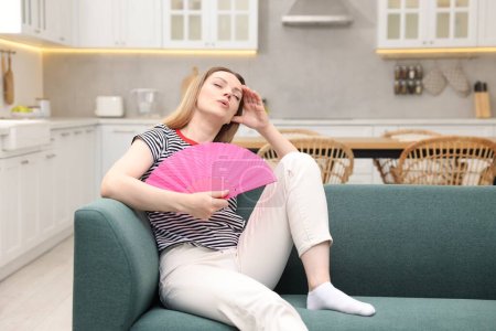 Foto de Mujer agitando ventilador de mano rosa para refrescarse en el sofá en casa. Espacio para texto - Imagen libre de derechos
