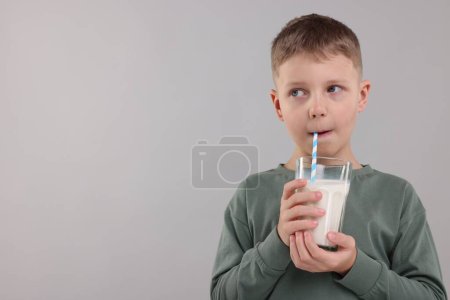 Téléchargez les photos : Mignon garçon boire du lait frais à partir de verre sur fond gris clair, espace pour le texte - en image libre de droit