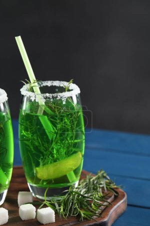 Photo for Glass of homemade refreshing tarragon drink, sprigs and sugar cubes on blue wooden table - Royalty Free Image