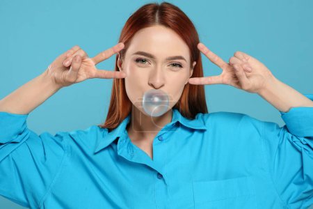 Photo for Beautiful woman blowing bubble gum and gesturing on turquoise background - Royalty Free Image