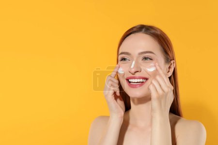 Photo for Beautiful young woman with sun protection cream on her face against orange background, space for text - Royalty Free Image