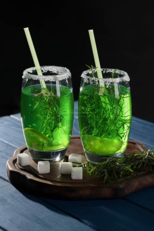 Photo for Glasses of homemade refreshing tarragon drink, sprigs and sugar cubes on blue wooden table - Royalty Free Image