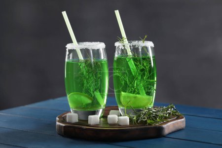 Photo for Glasses of homemade refreshing tarragon drink, sprigs and sugar cubes on blue wooden table - Royalty Free Image