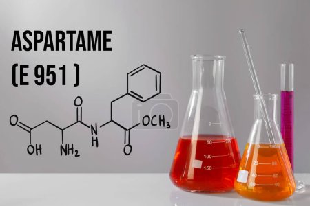 Téléchargez les photos : Formule chimique structurelle de l'aspartame (E951) et verrerie de laboratoire avec liquides sur table grise - en image libre de droit