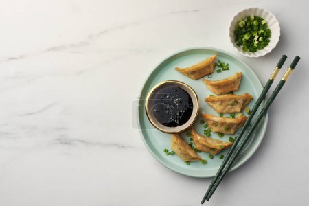 Téléchargez les photos : Délicieux gyoza (boulettes asiatiques) avec sauce soja, oignons verts et baguettes sur table en marbre blanc, plat. Espace pour le texte - en image libre de droit