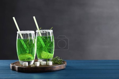 Photo for Glasses of homemade refreshing tarragon drink, sprigs and sugar cubes on blue wooden table, space for text - Royalty Free Image