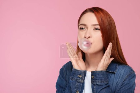 Téléchargez les photos : Portrait de belle femme soufflant de la gomme à bulles sur fond rose. Espace pour le texte - en image libre de droit