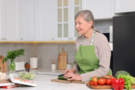 Foto de Mujer mayor cocinando por libro de recetas en la cocina - Imagen libre de derechos