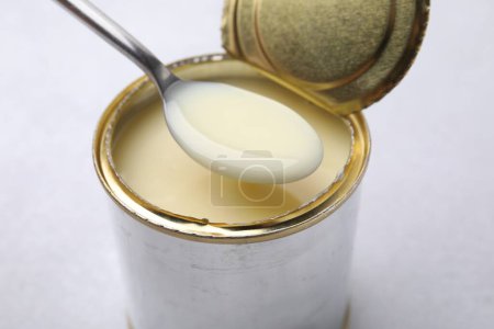 Téléchargez les photos : Cuillère avec du lait condensé sur une boîte ouverte sur une table blanche, gros plan - en image libre de droit